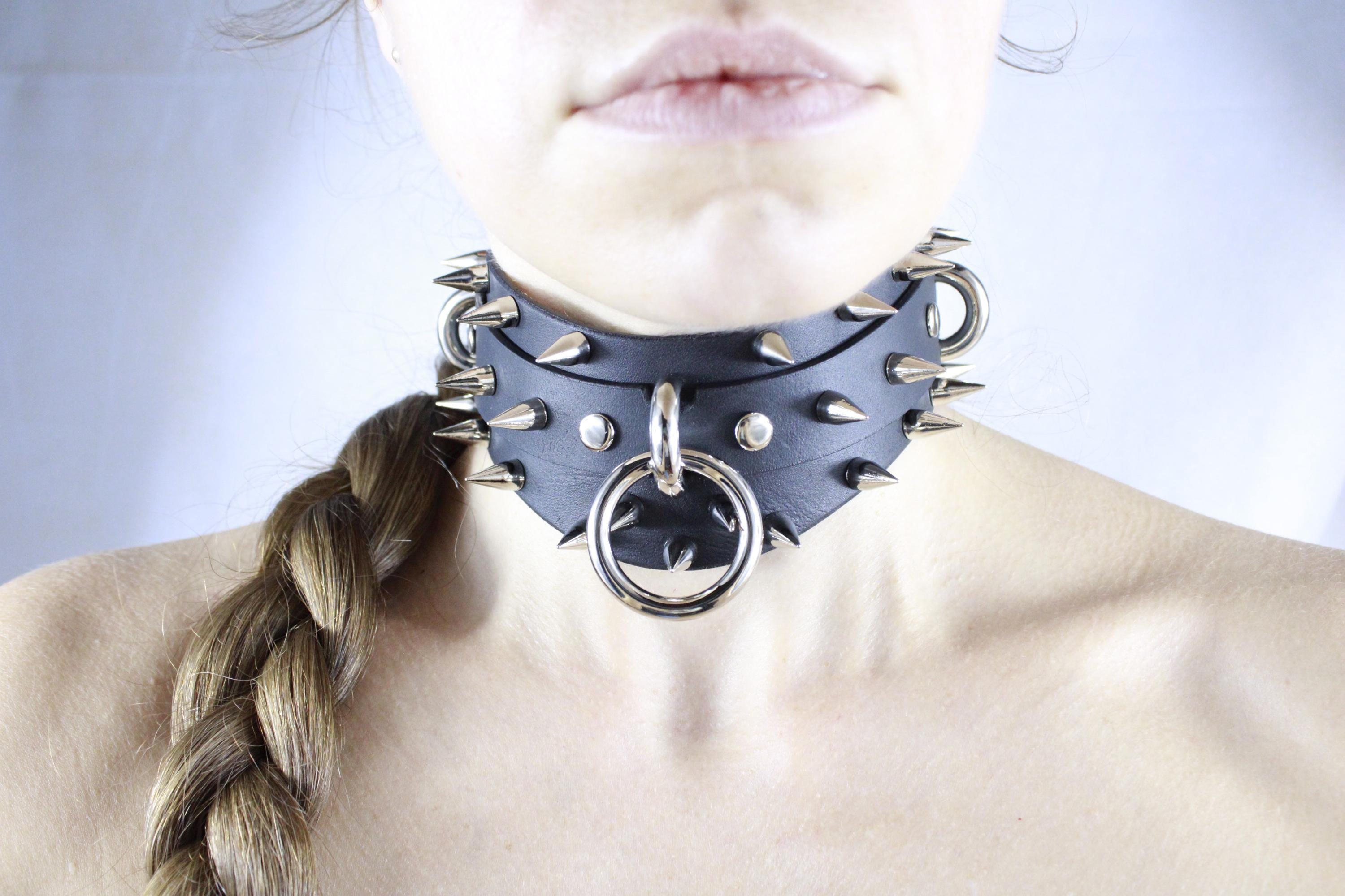 A close-up of a person's neck and chin wearing a black leather choker necklace with spikes and a ring.