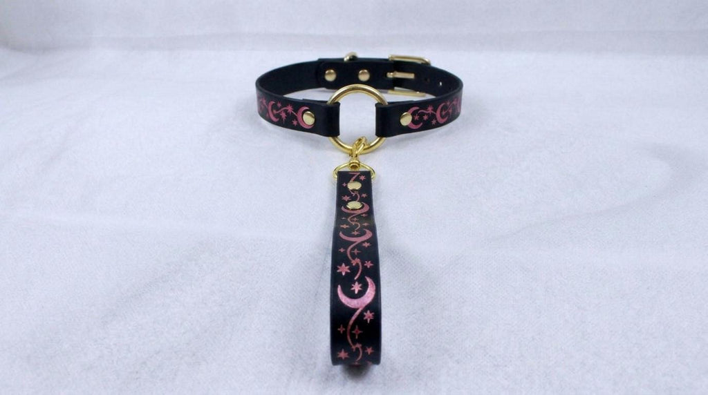 A black collar with a gold buckle and a pink and black floral design on the strap.