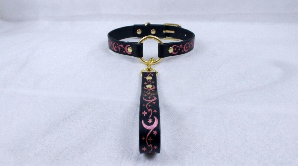 A black collar with a gold buckle and a pink and black floral design on the strap.