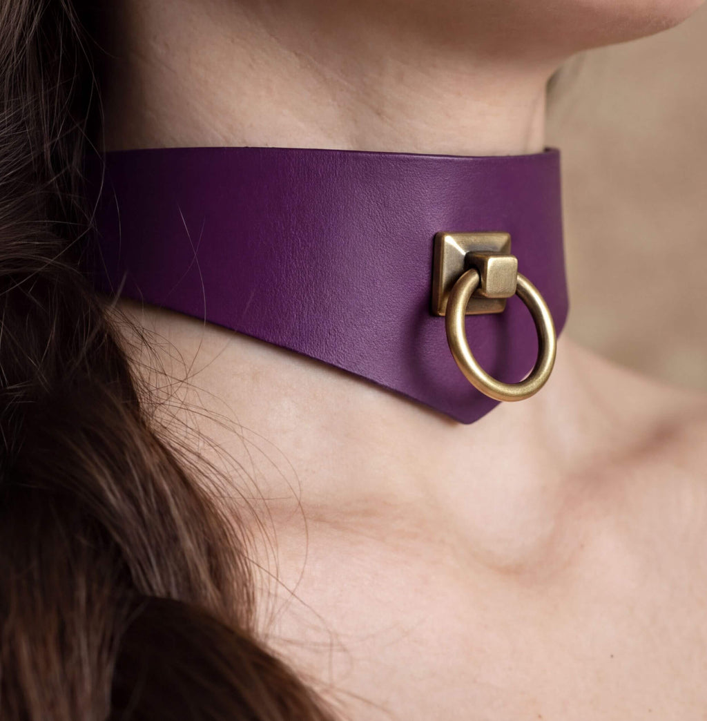 A close-up view of a person's neck and chin area, featuring a purple choker necklace with a gold-colored metal ring.
