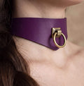 A close-up view of a person's neck and chin area, featuring a purple choker necklace with a gold-colored metal ring.