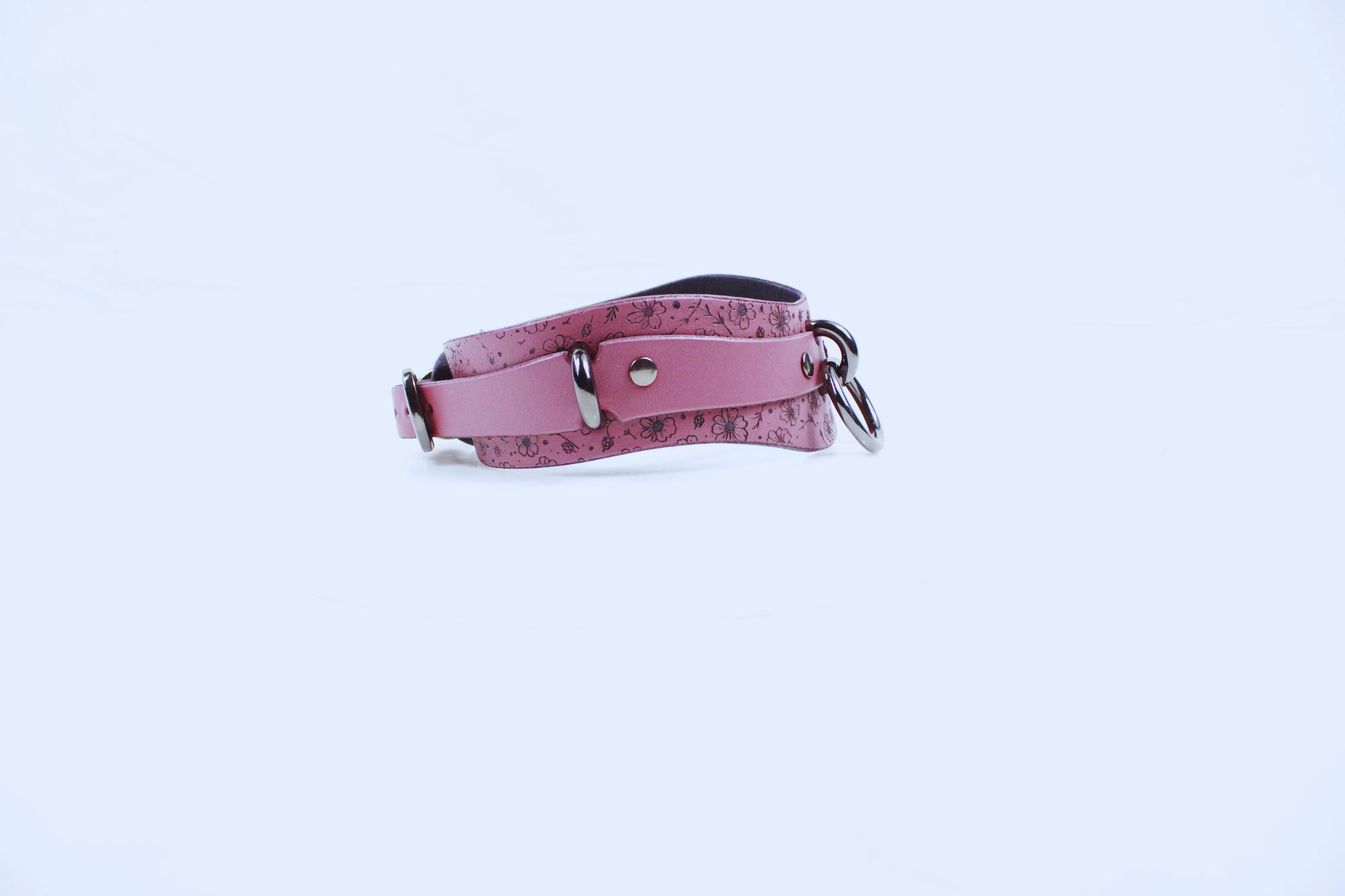 A pink leather strap with metal hardware, such as buckles and clips, is shown against a plain white background.