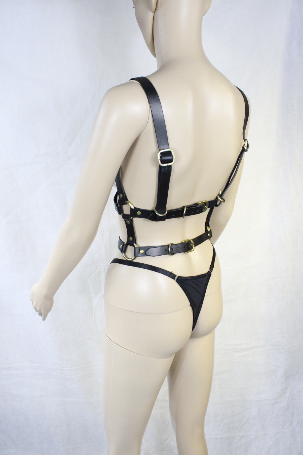 A mannequin wearing a black leather harness with straps and buckles.