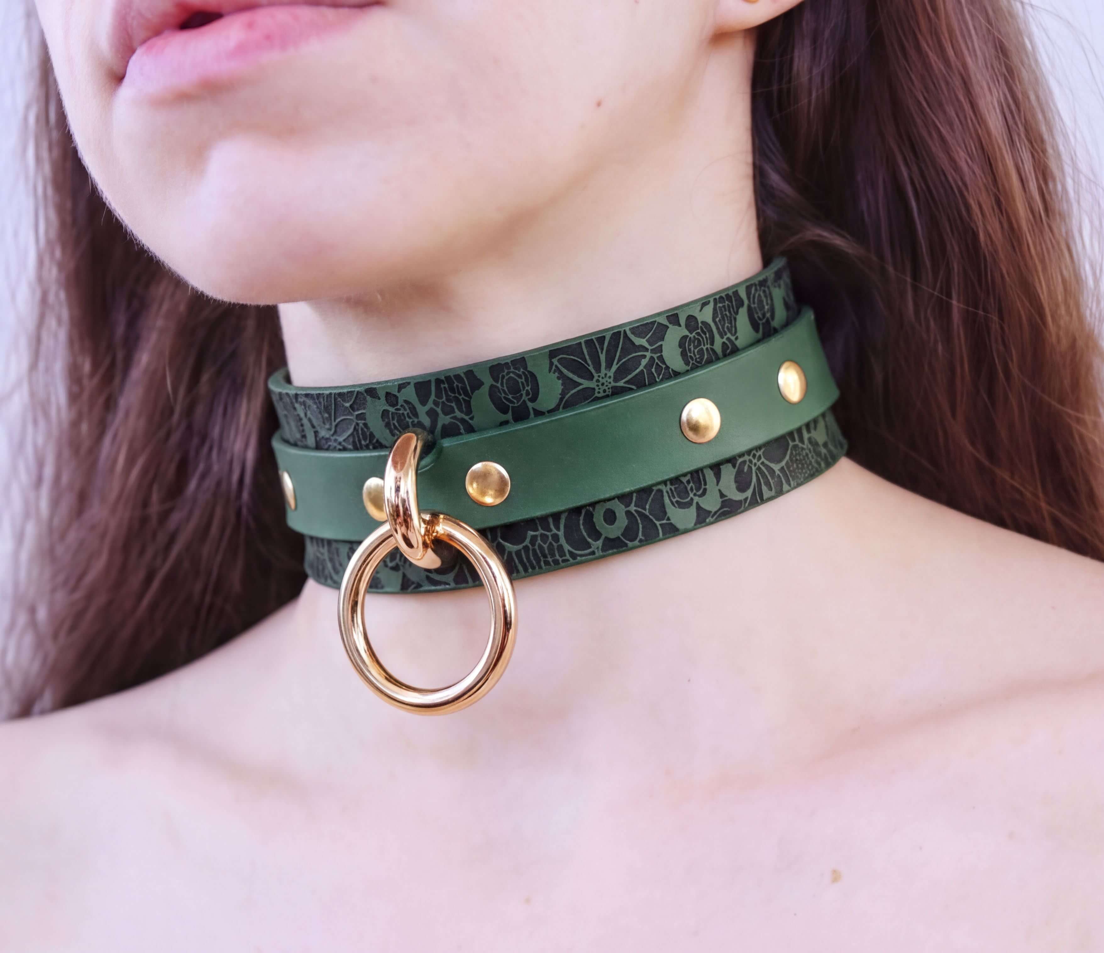 A close-up of a person's neck wearing a green leather choker necklace with a gold ring and studs.