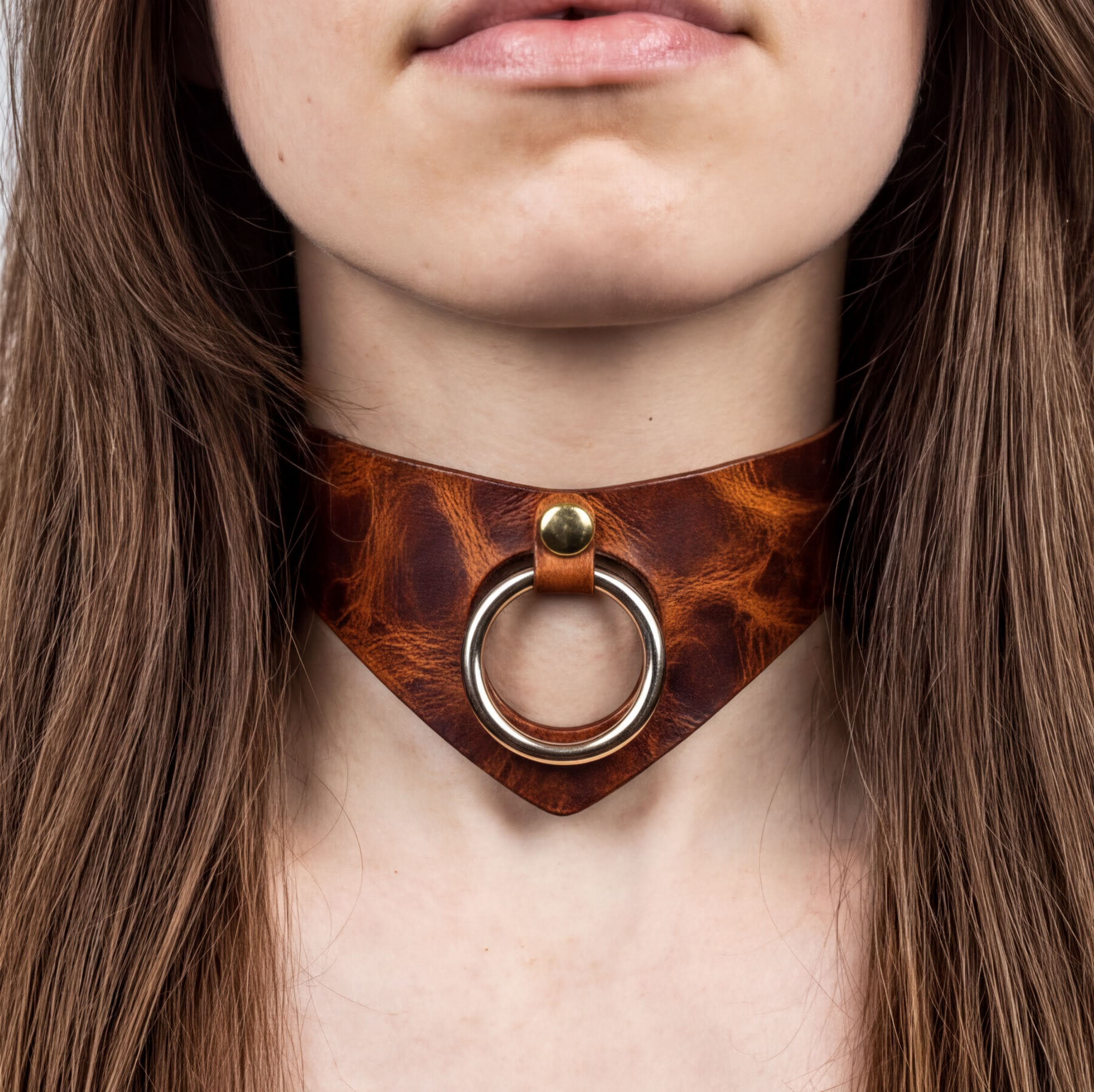A close-up of a woman's neck and chest area, featuring a leather choker necklace with a metal ring and a gold-colored buckle.