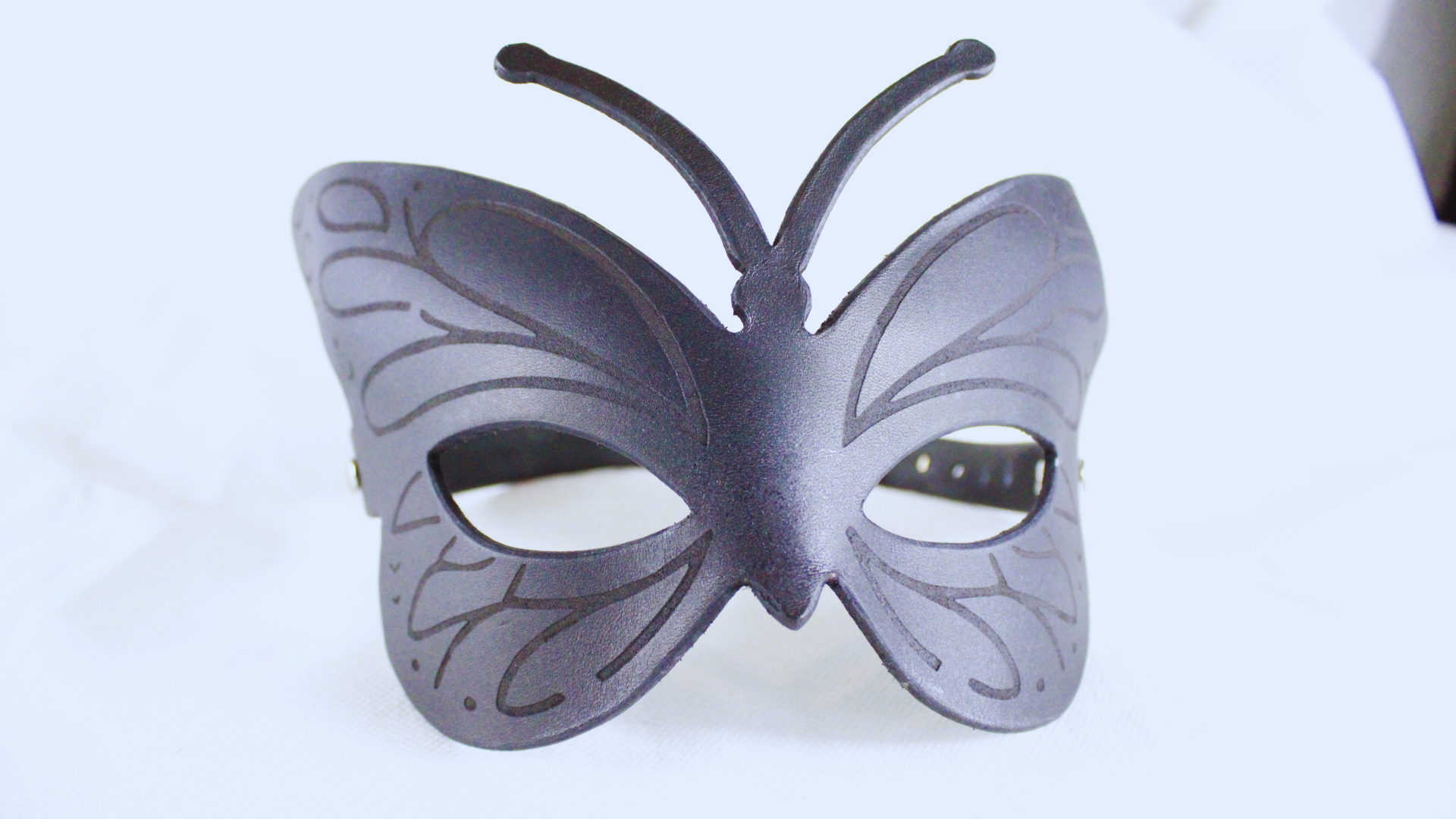 A black butterfly-shaped mask with intricate designs on the wings and body.
