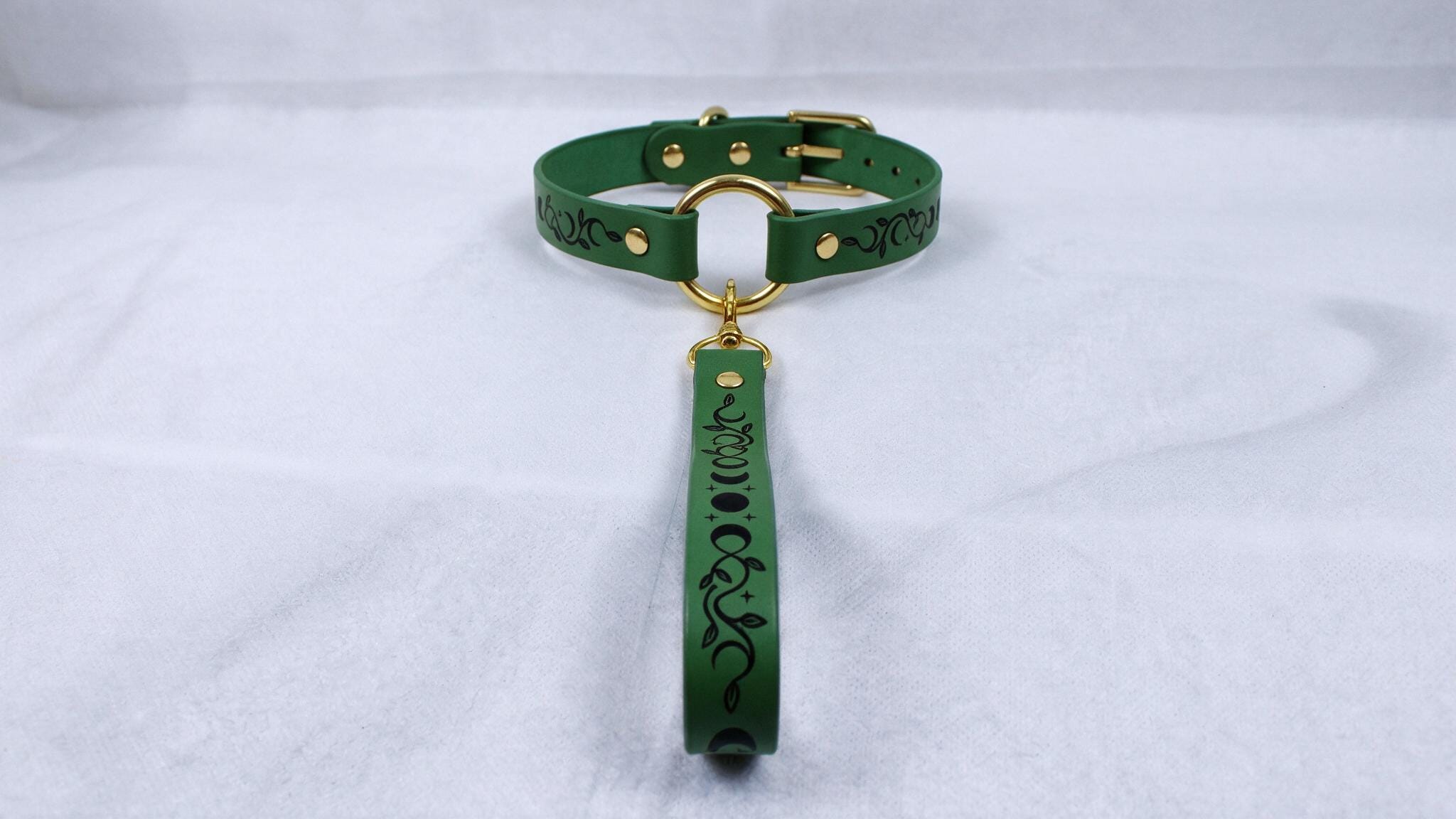 A green collar with a gold buckle and a black and white floral design on the handle.