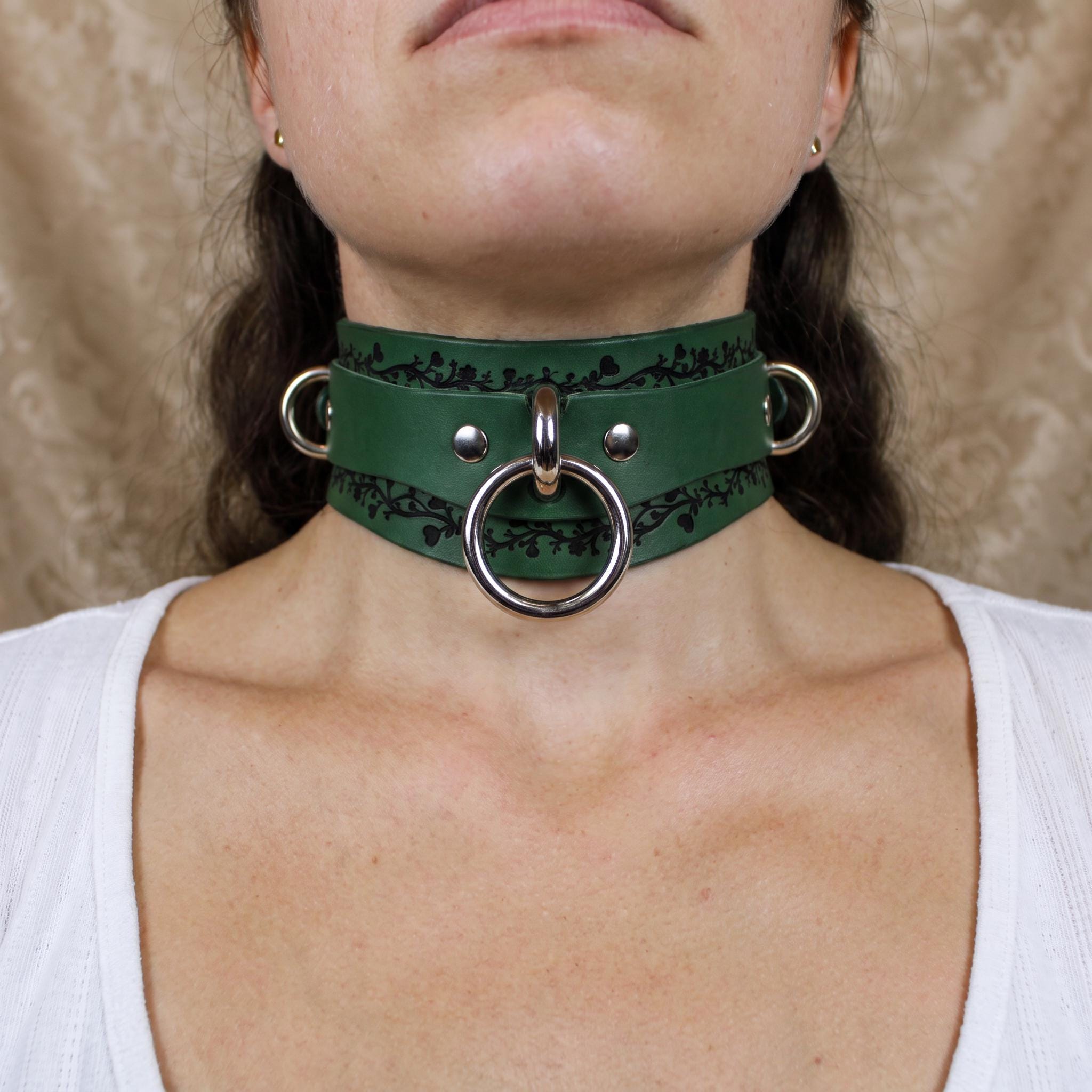 A close-up of a woman's neck wearing a green leather choker necklace with metal rings and a metal ring on the front.