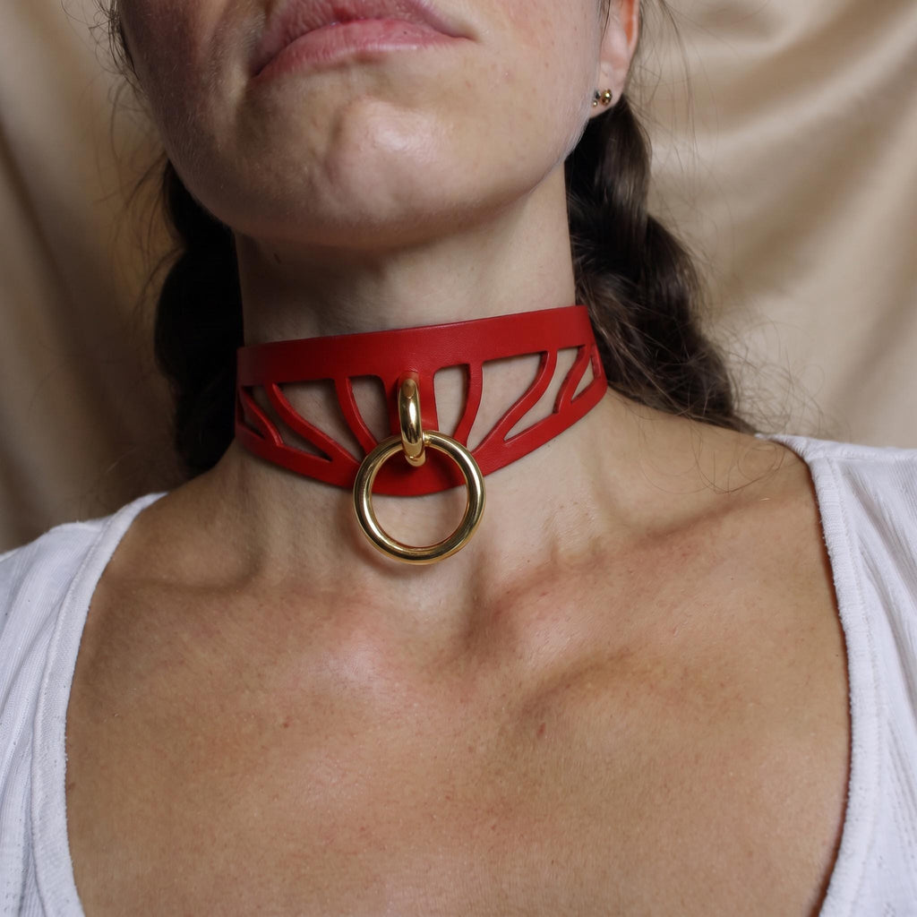 A close-up of a woman's neck wearing a red choker necklace with a gold ring.