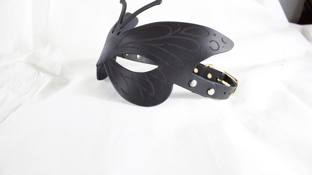 A black butterfly-shaped mask with a decorative design and a black leather strap.