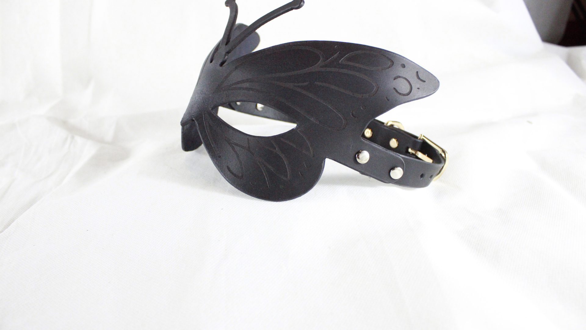A black butterfly-shaped mask with a decorative design and a black leather strap.
