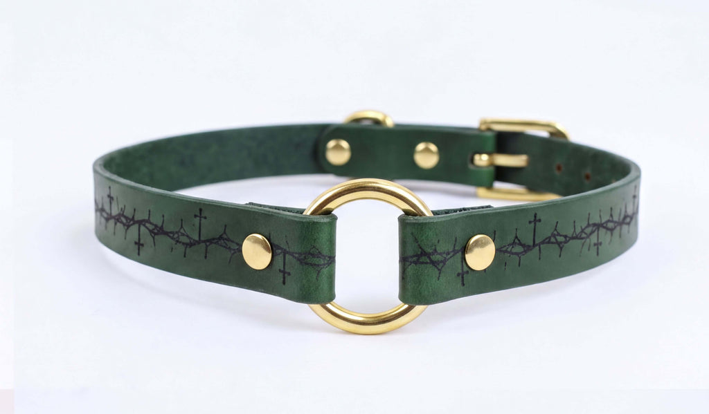 A green leather collar with a gold-colored metal ring and a decorative pattern on the strap.