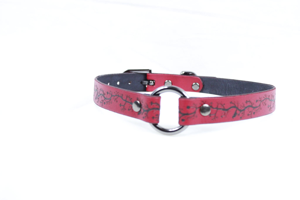 A red leather collar with a black floral pattern and a metal ring on the front.