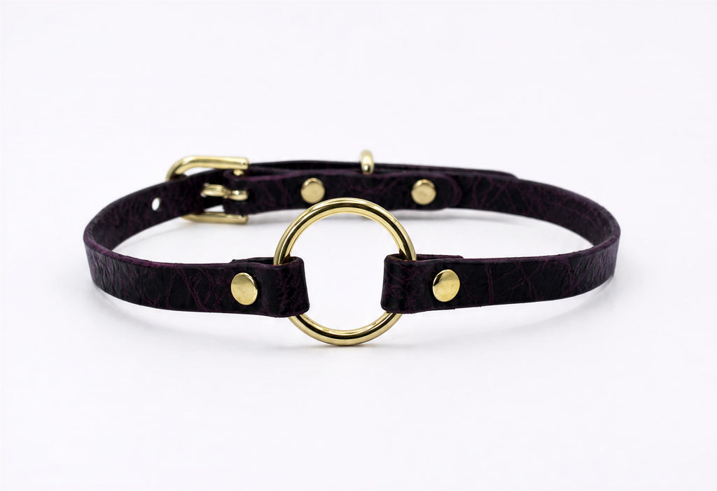 A purple leather choker collar with a gold-colored metal ring and three gold-colored metal fasteners.