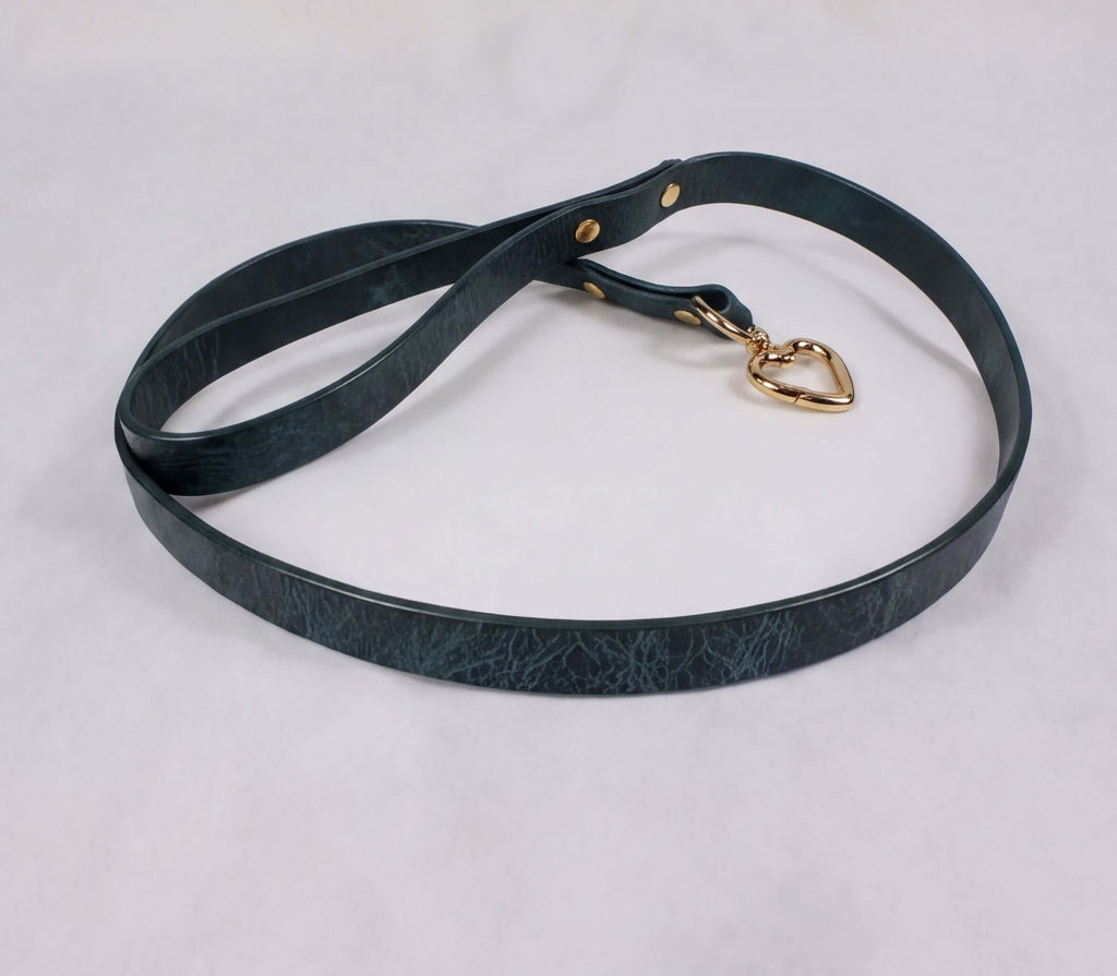A dark green leather leash with a gold heart-shaped tag attached, resting on a white surface.