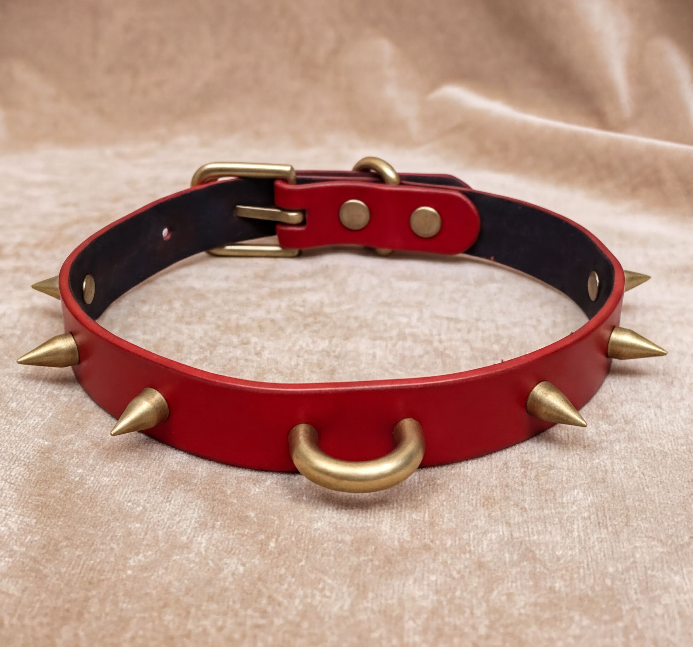 A red leather dog collar with spikes on it, placed on a beige fabric background.