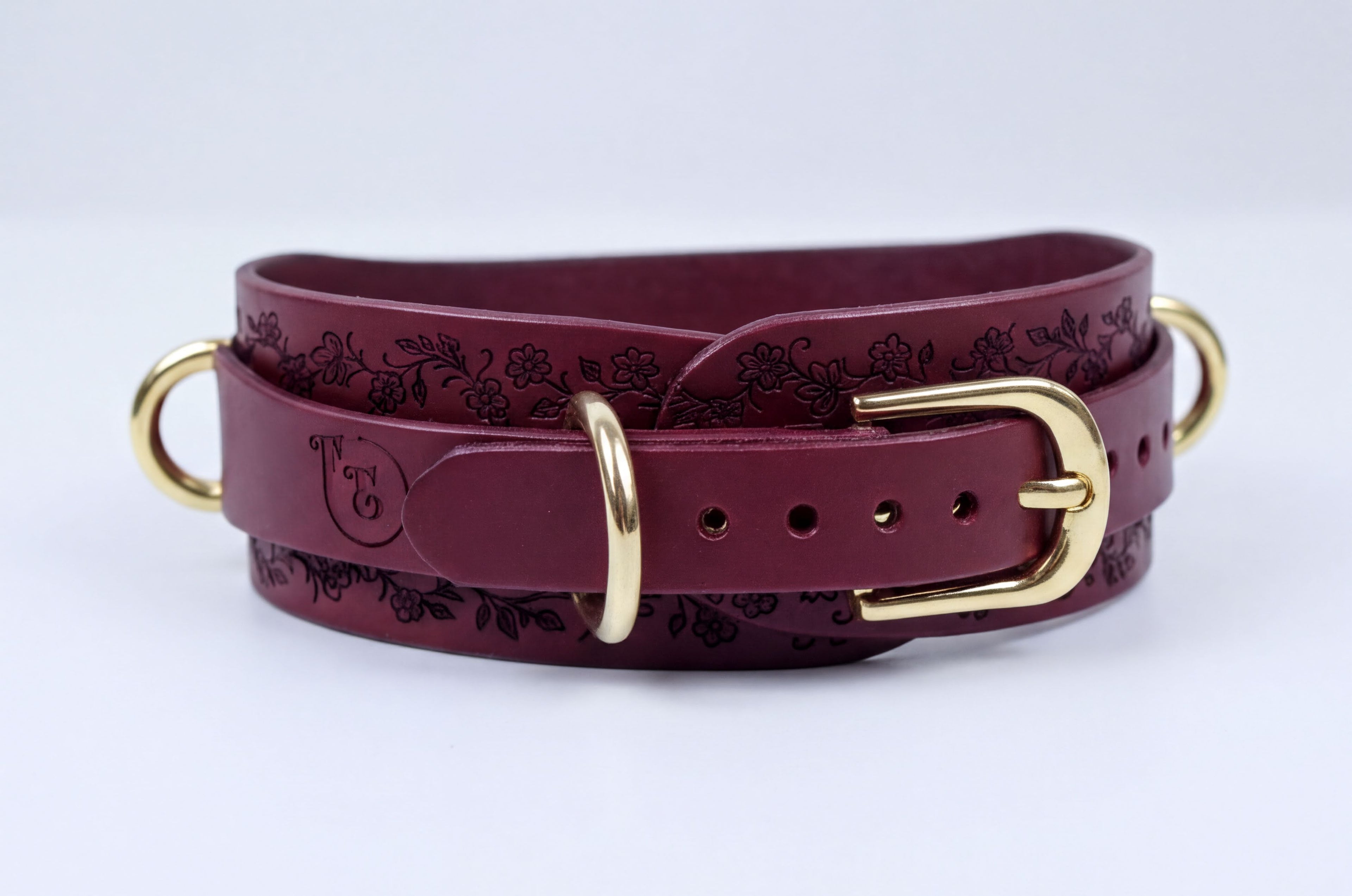 A burgundy leather belt with a gold buckle and two gold-colored holes on the front.