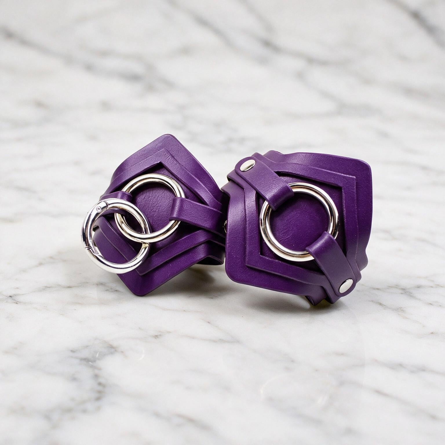 A pair of purple leather straps with metal rings, resting on a marble surface.
