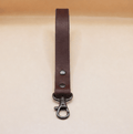 A brown leather strap with a metal clasp and hook attached to it.