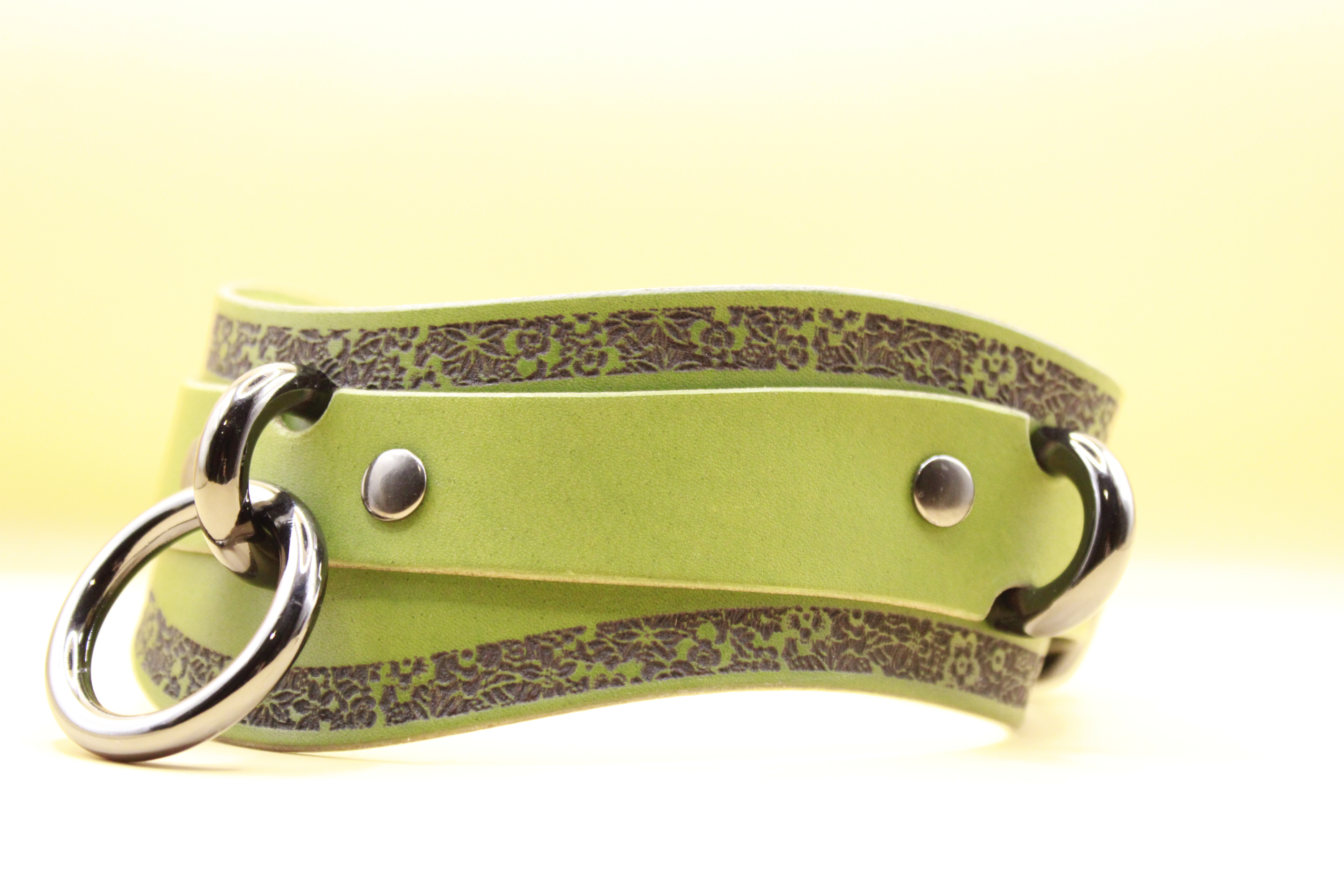 A green leather strap with metal rings and decorative patterns on it.