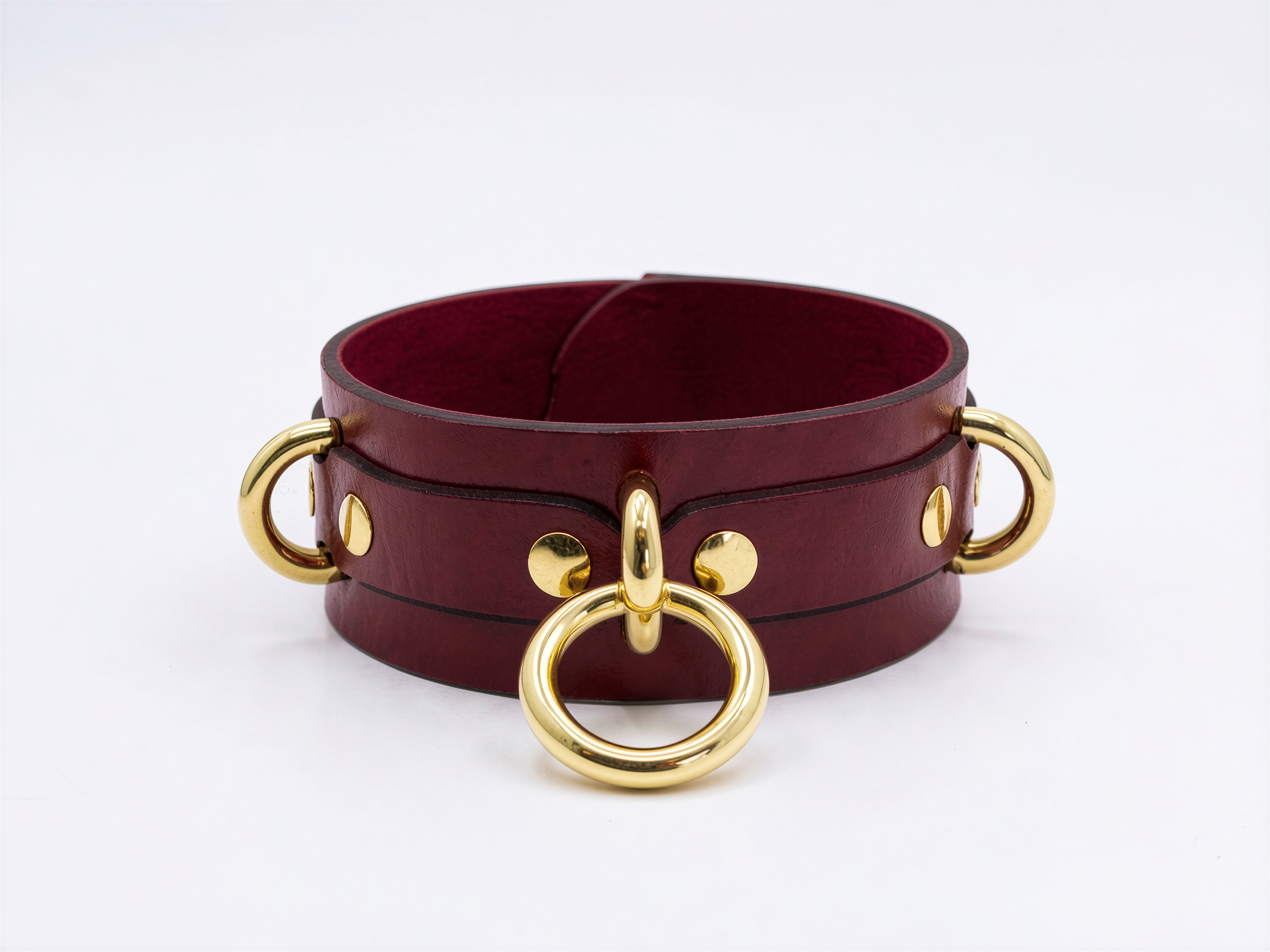 A burgundy leather choker necklace with gold-colored metal rings and buckles.