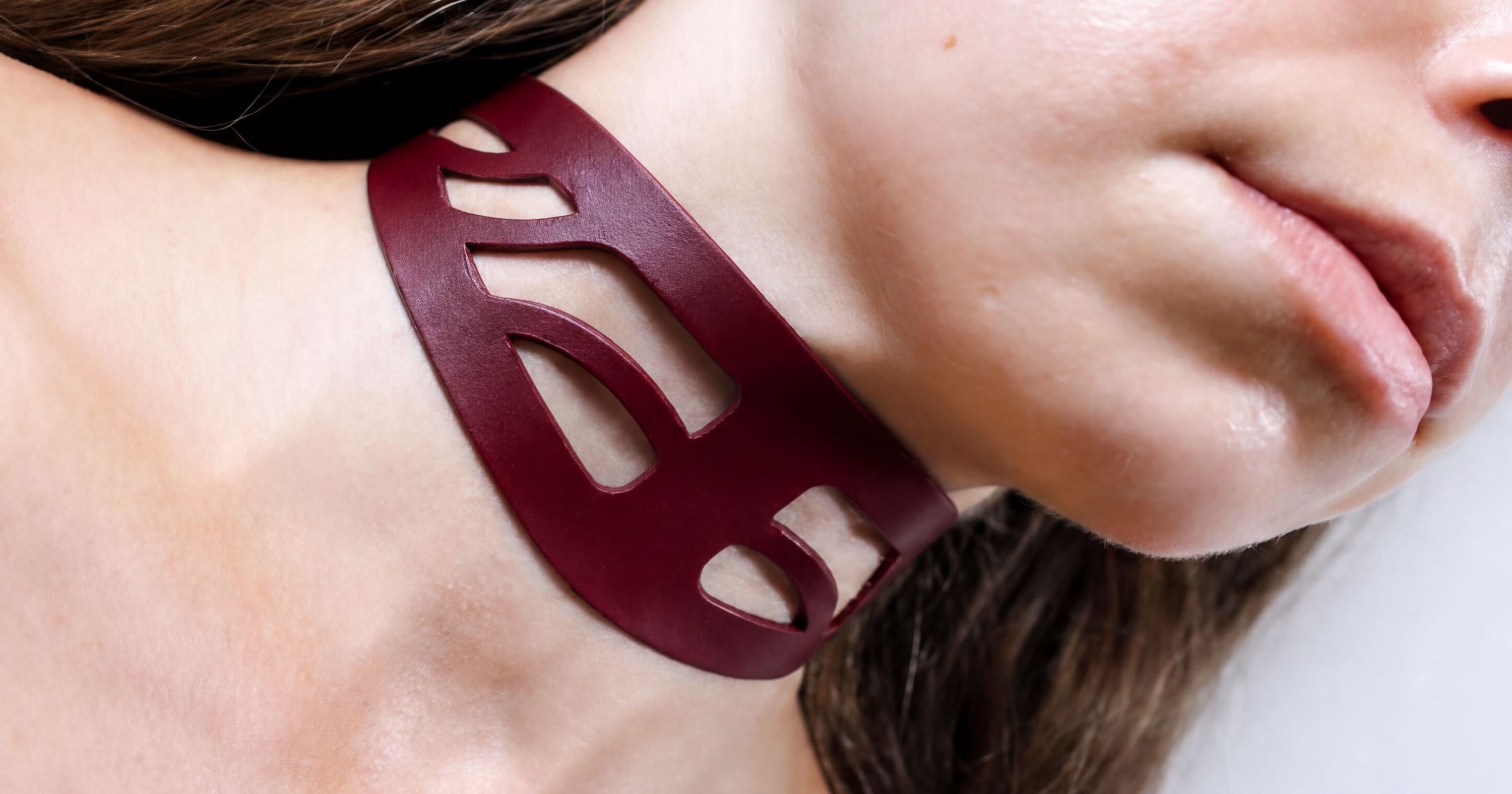 A close-up of a woman's neck and chin wearing a burgundy-colored leather choker necklace.