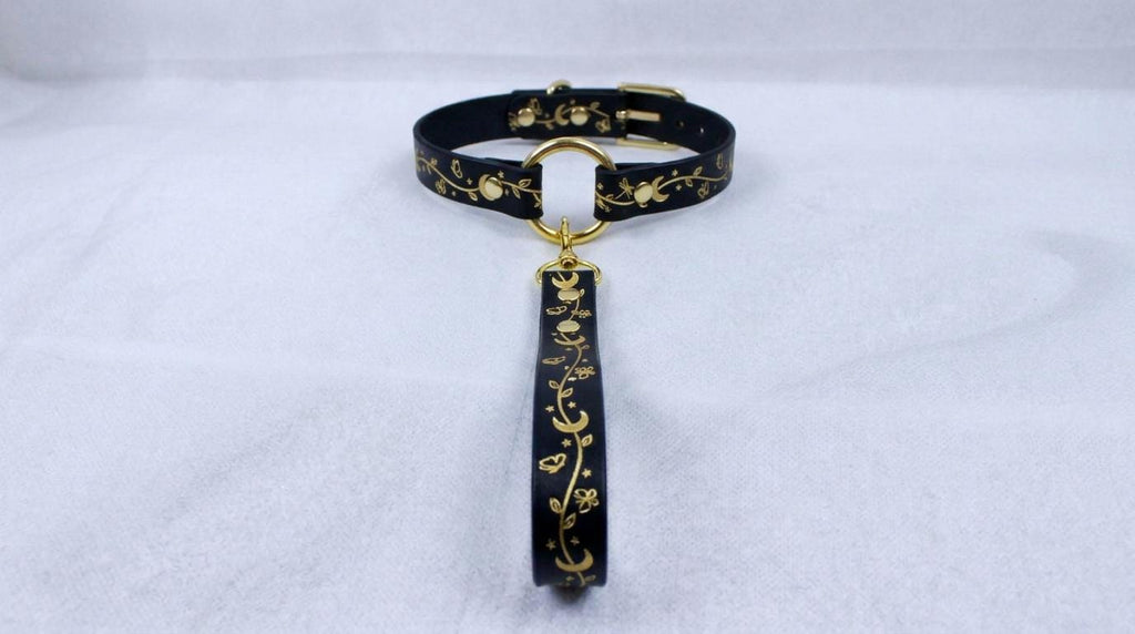 A black collar with a gold-colored pendant featuring a floral design.