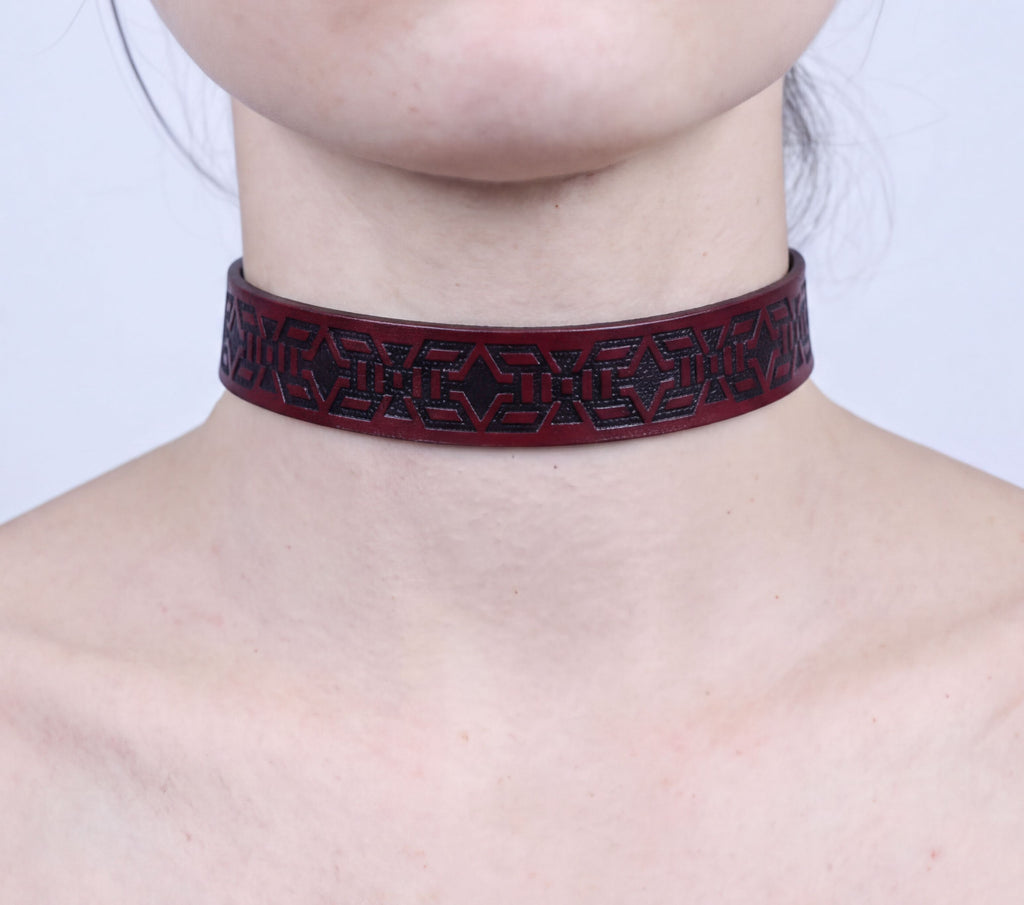 A close-up of a person's neck wearing a burgundy-colored choker necklace with a geometric pattern.