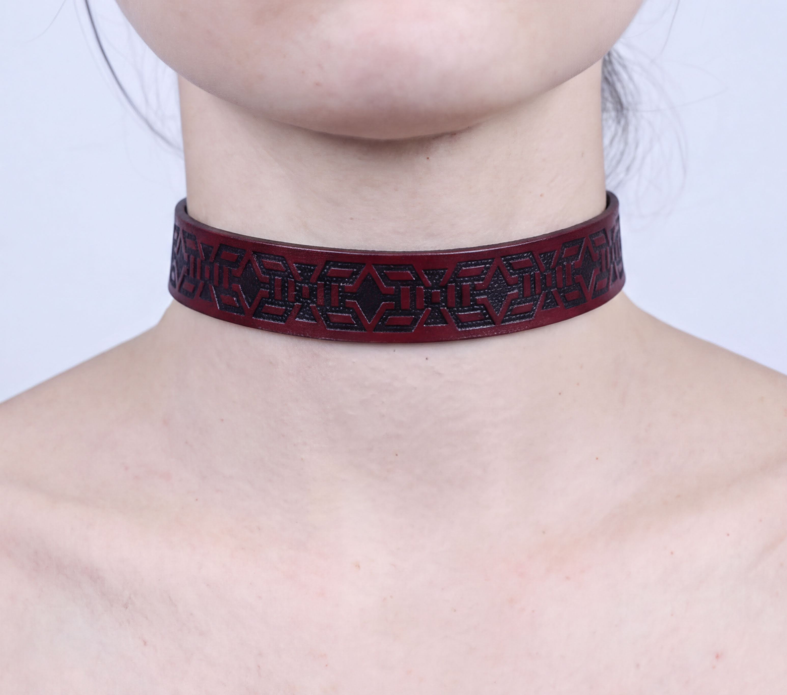 A close-up of a person's neck wearing a burgundy-colored choker necklace with a geometric pattern.