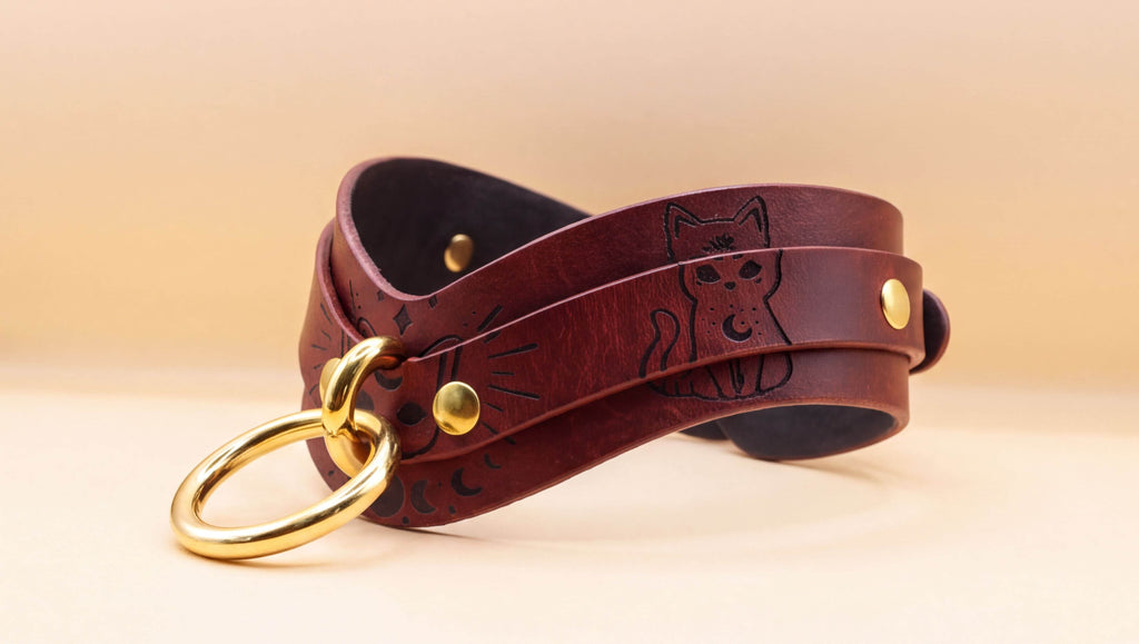 A brown leather choker necklace with a cat design and a gold ring.
