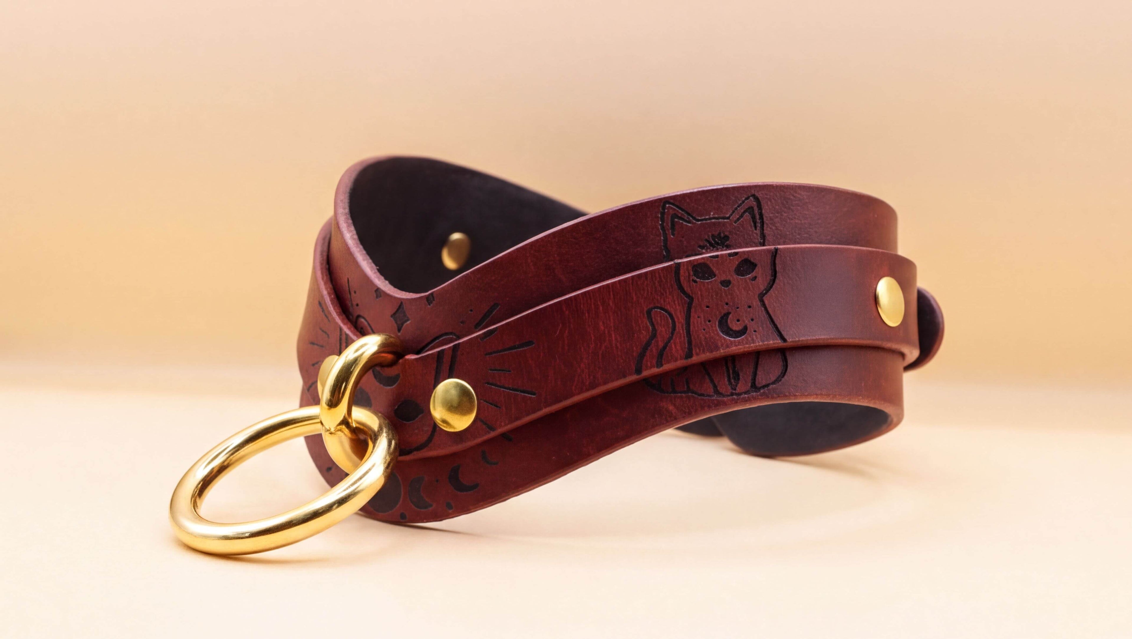 A brown leather choker necklace with a cat design and a gold ring.