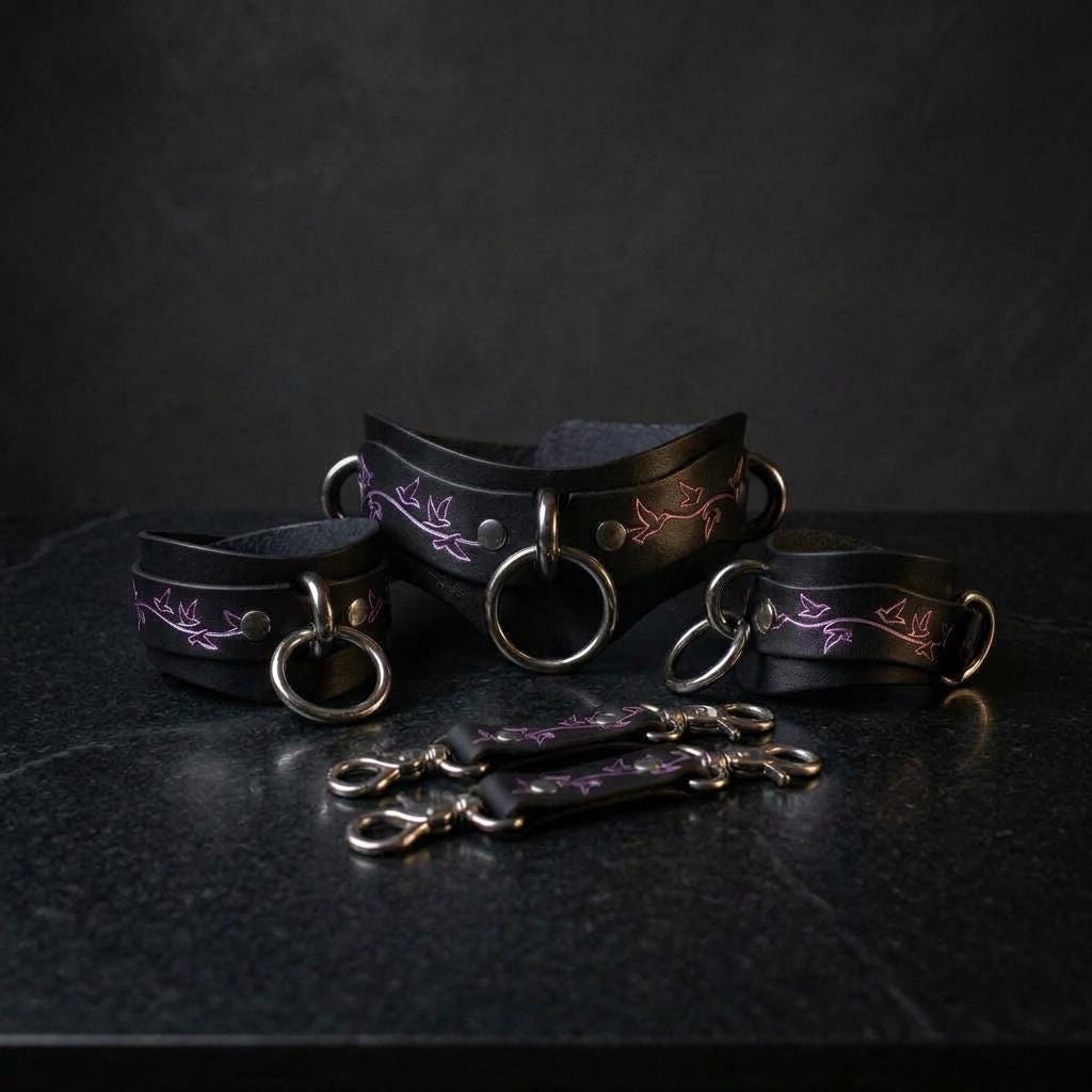 a set of black leather restraints with purple floral designs, arranged on a dark surface.