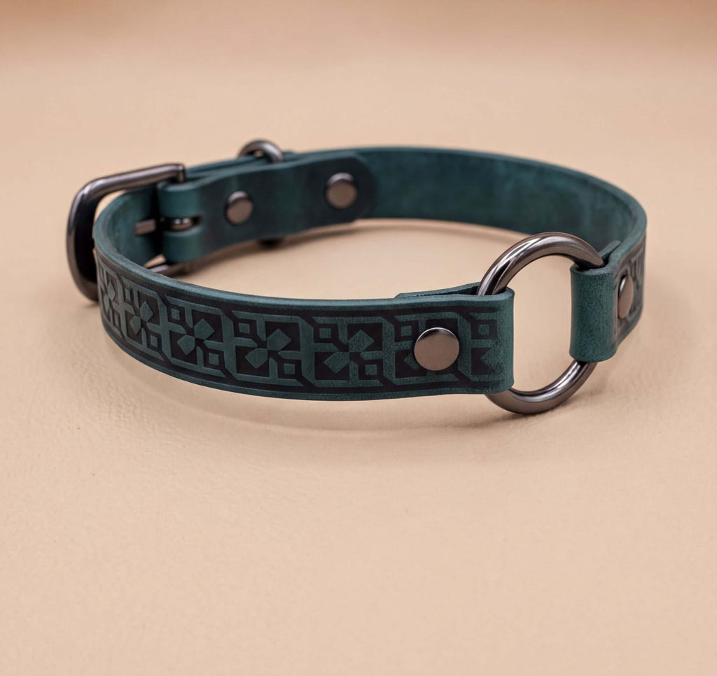 A green leather dog collar with metal rings and a decorative pattern on the strap.