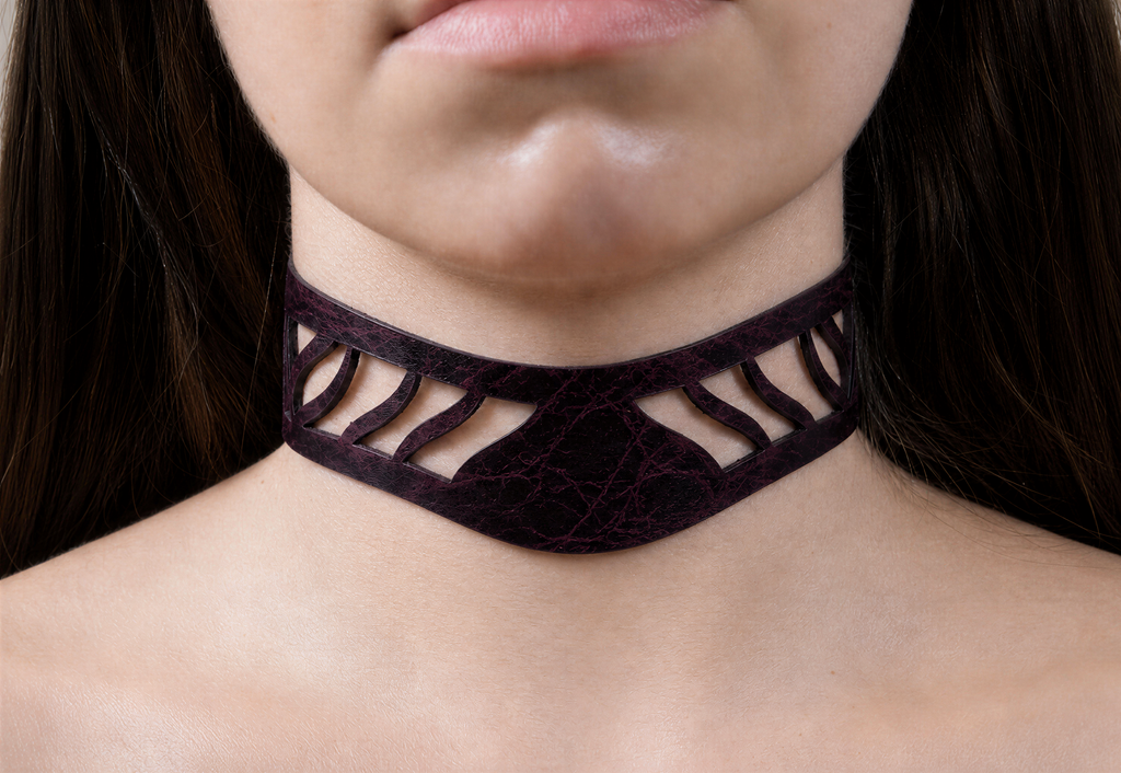 A close-up of a woman's neck and chin area, featuring a choker-style necklace with a dark purple or burgundy-colored design.