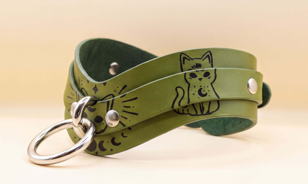 A green leather choker necklace with a cat design and a metal ring.