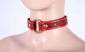 A mannequin head wearing a red leather choker necklace with a gold ring and heart-shaped embellishments.