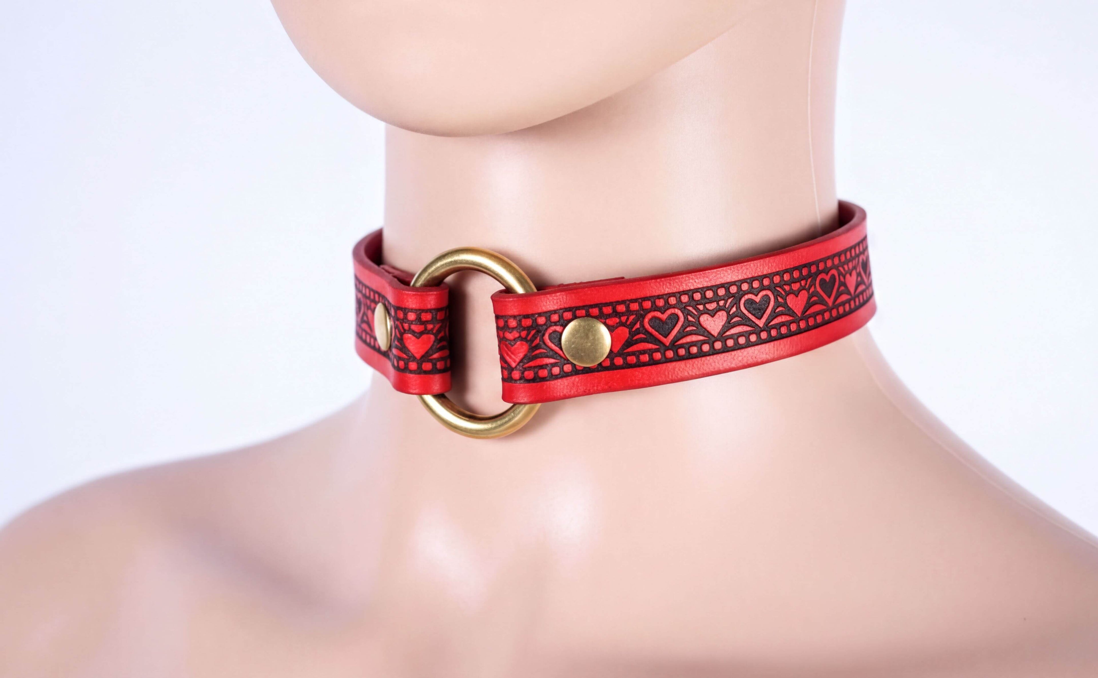 A mannequin head wearing a red leather choker necklace with a gold ring and heart-shaped embellishments.