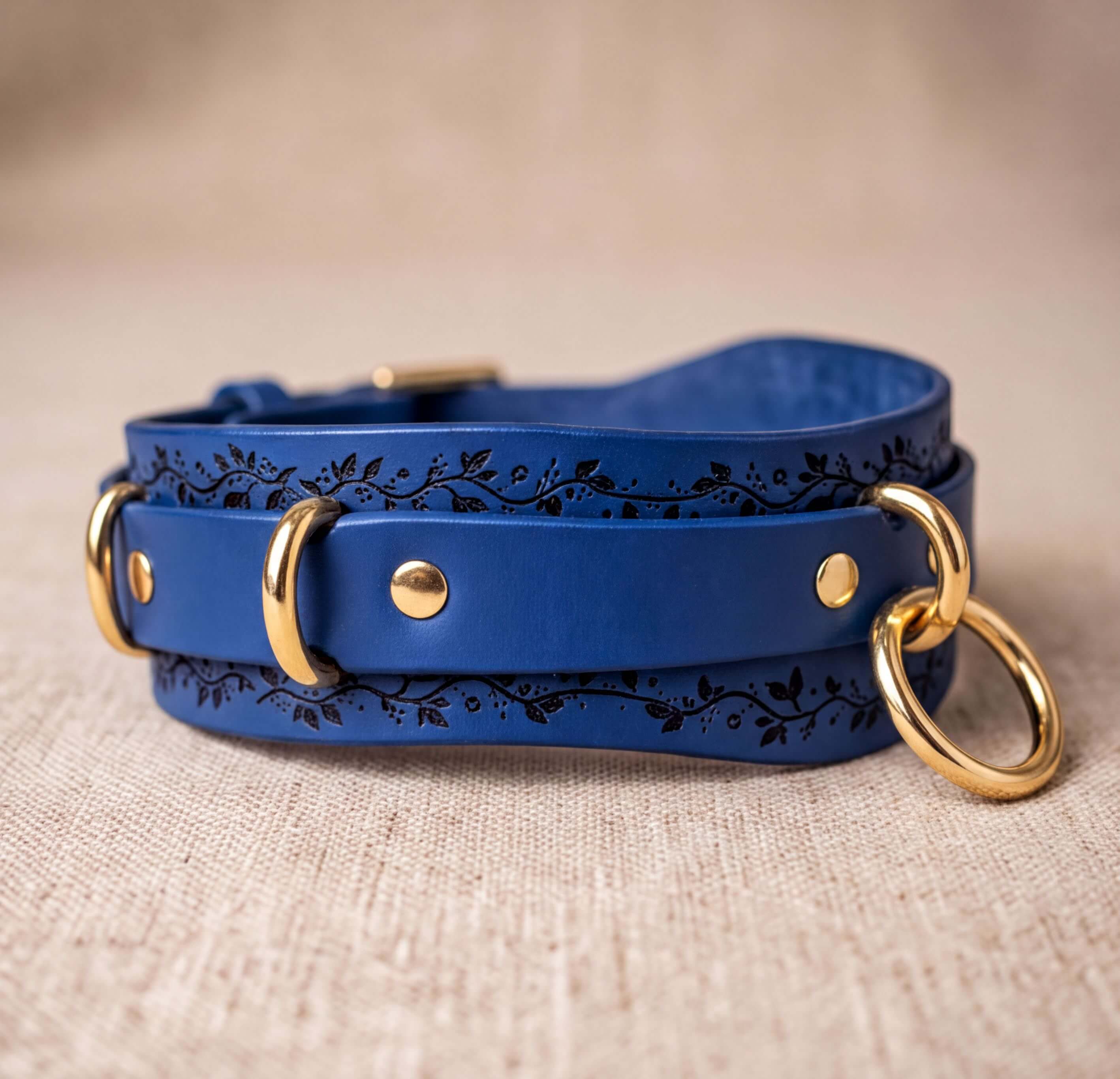A blue leather dog collar with gold metal rings and decorative elements on the surface.