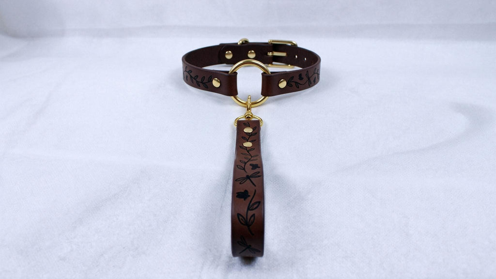 A brown leather collar with a gold buckle and a black handle with a floral design.