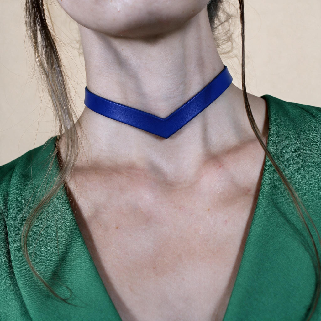 A close-up of a woman's neck wearing a blue choker necklace against a green blouse.