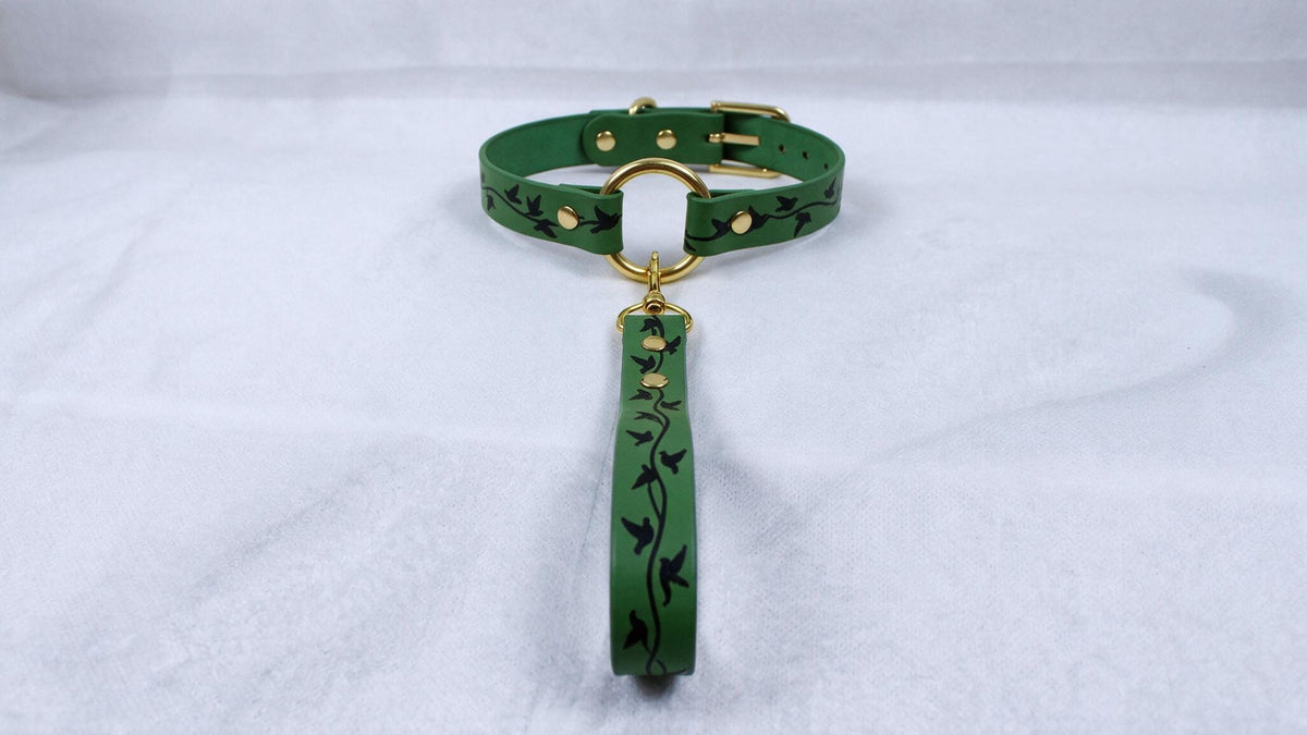 A green leather collar with a gold-colored buckle and a green leash attached to it, resting on a white surface.