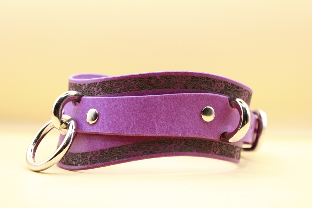 A purple leather choker necklace with metal rings and a decorative pattern on the front.