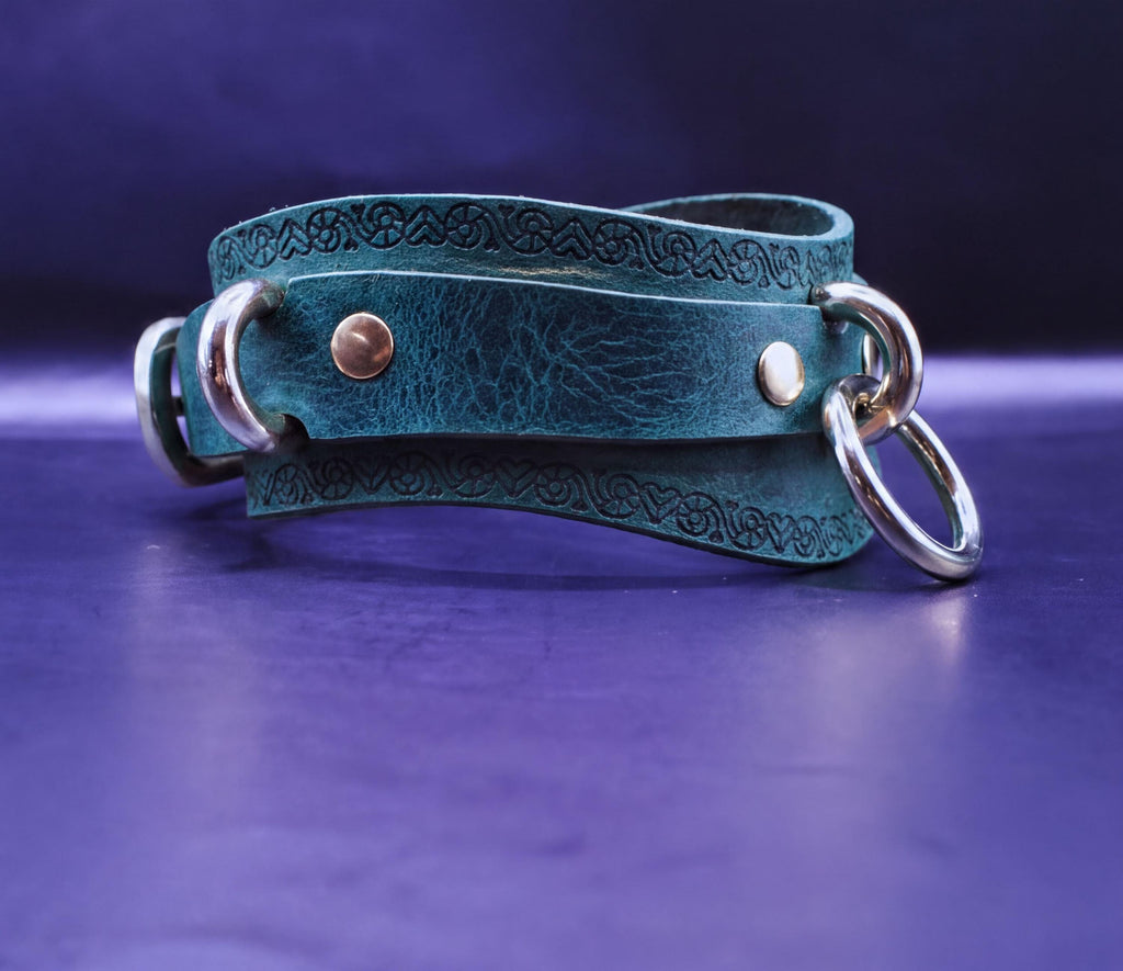 A green leather choker necklace with metal rings and a decorative pattern on the clasp is displayed against a dark purple background.
