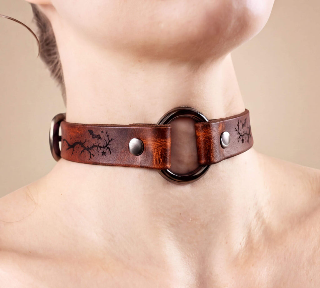 A close-up image of a person wearing a brown leather choker necklace with a circular metal ring.