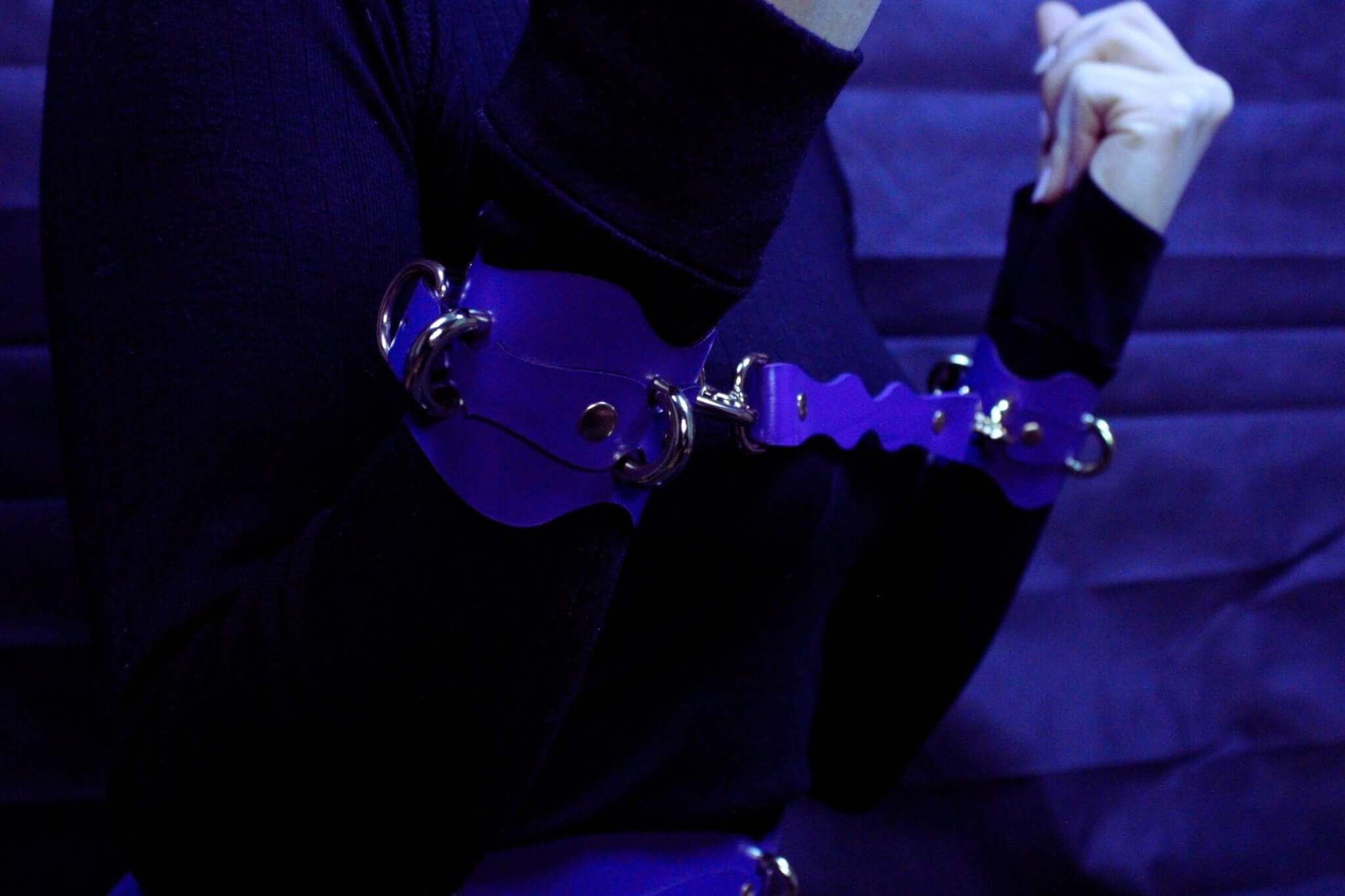 Handmade purple leather wrist cuffs with metal connectors, perfect for BDSM bondage gear and submissive accessories.