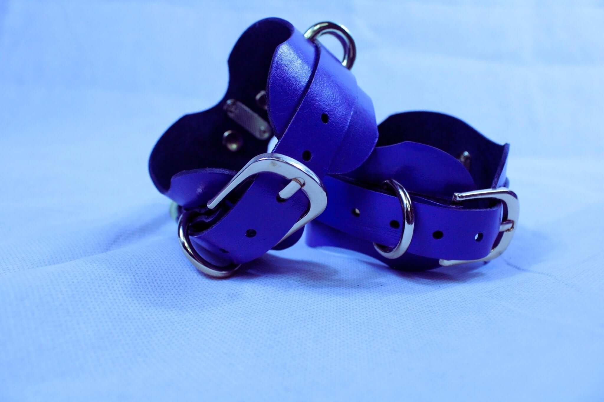 Handmade royal blue leather wrist cuffs with sturdy connectors for BDSM restraint and kink, crafted for comfort and durability.