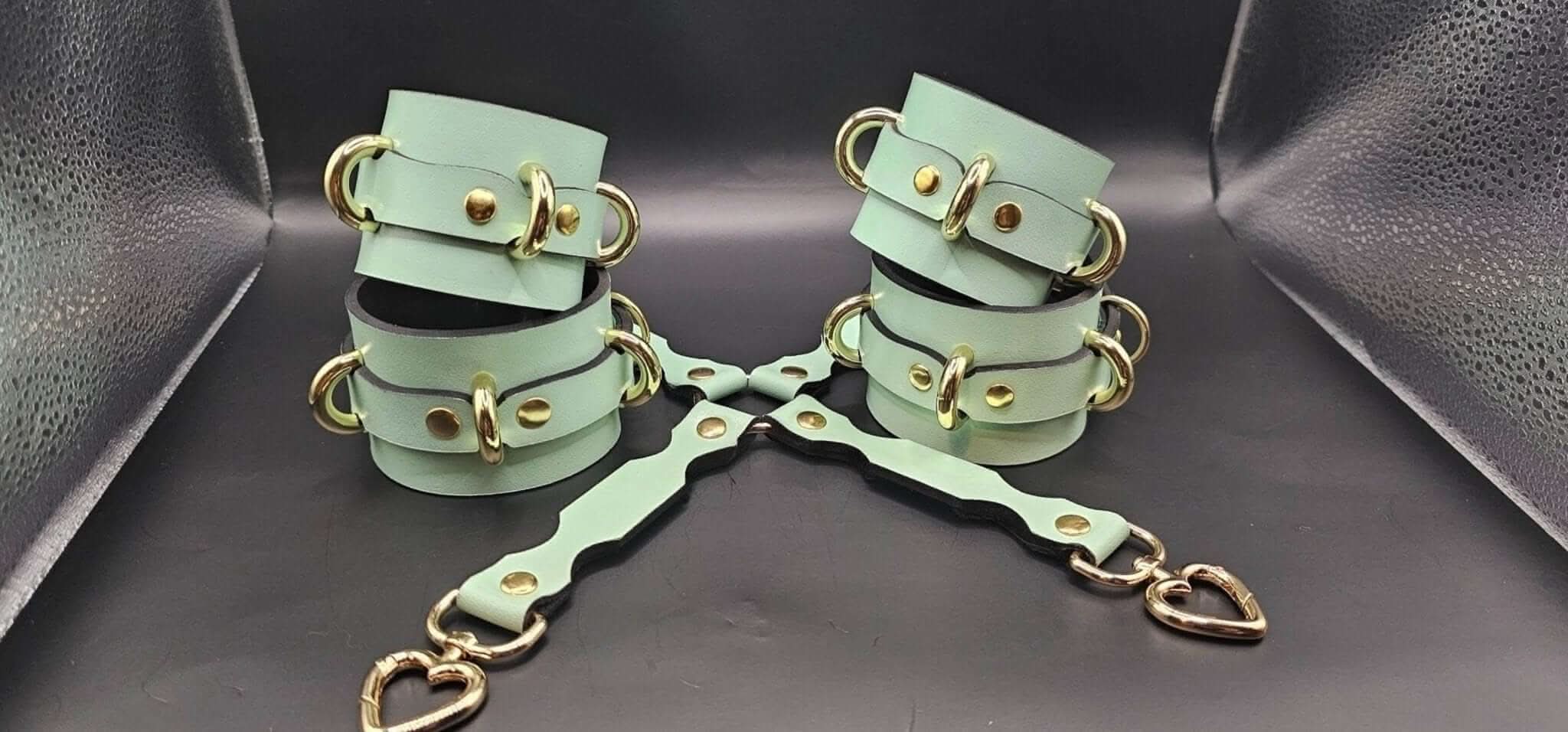 Handmade leather cuffs in mint green with gold hardware, perfect for BDSM bondage play and adjustable for wrist or ankle restraint.