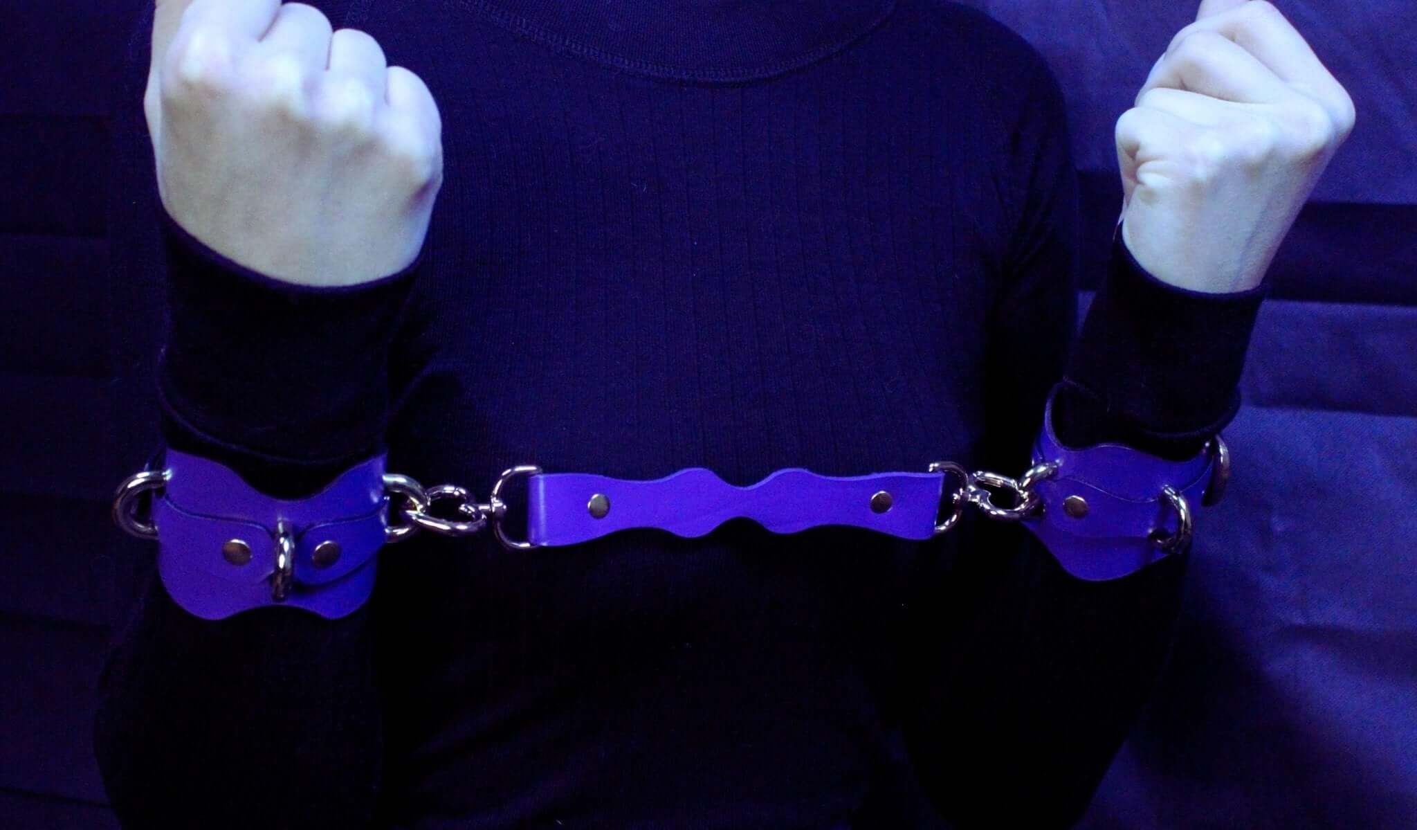 Purple leather wrist cuffs connected for restraint, perfect for BDSM play and submissive accessories.