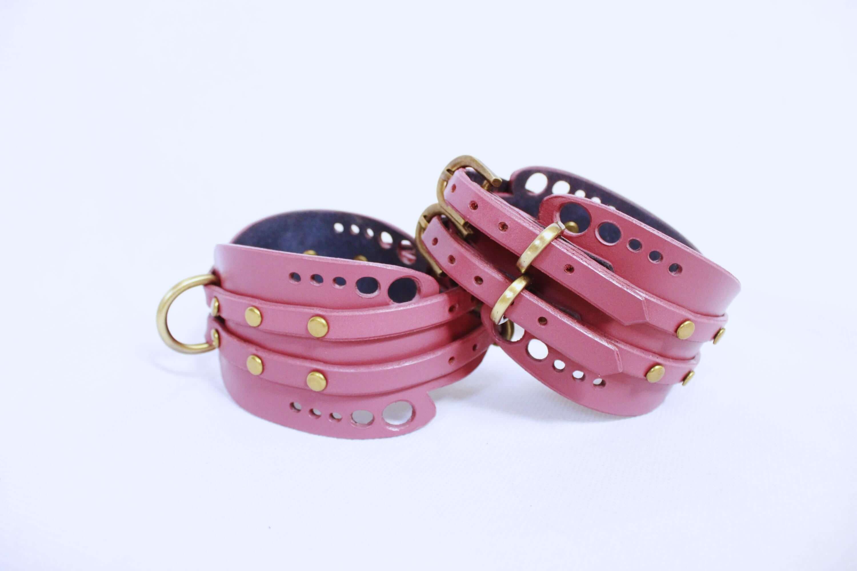 Mauve leather wrist cuffs set with brass hardware for BDSM submissive play and bondage gear.