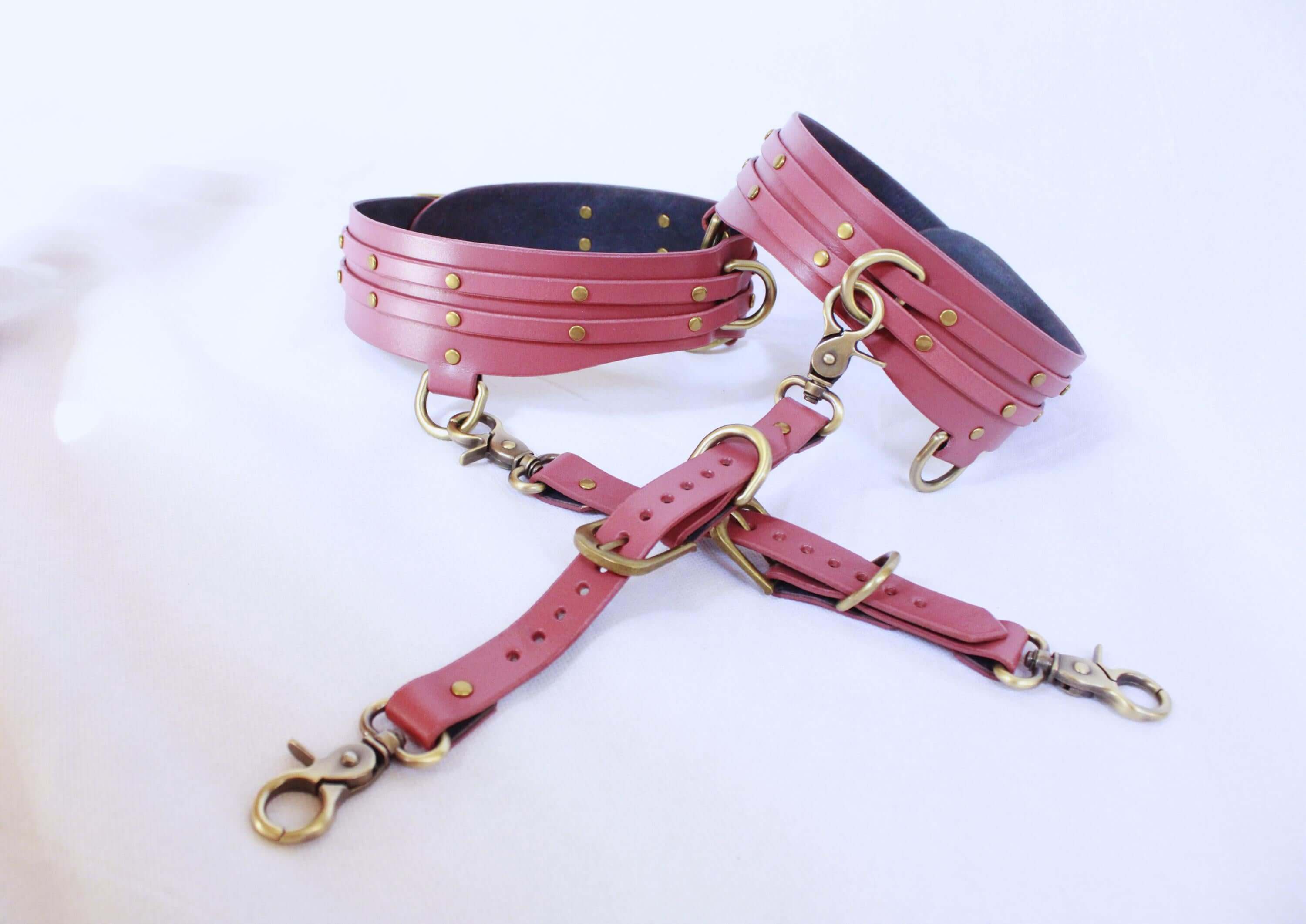 Adjustable pink leather thigh cuffs set with metal fittings for BDSM bondage gear and submissive play.
